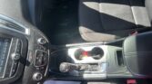 Interior of a car showing the center console with controls, gear shifter, and cup holder area; passenger seat and dashboard visible with sunlight casting shadows on the seat.