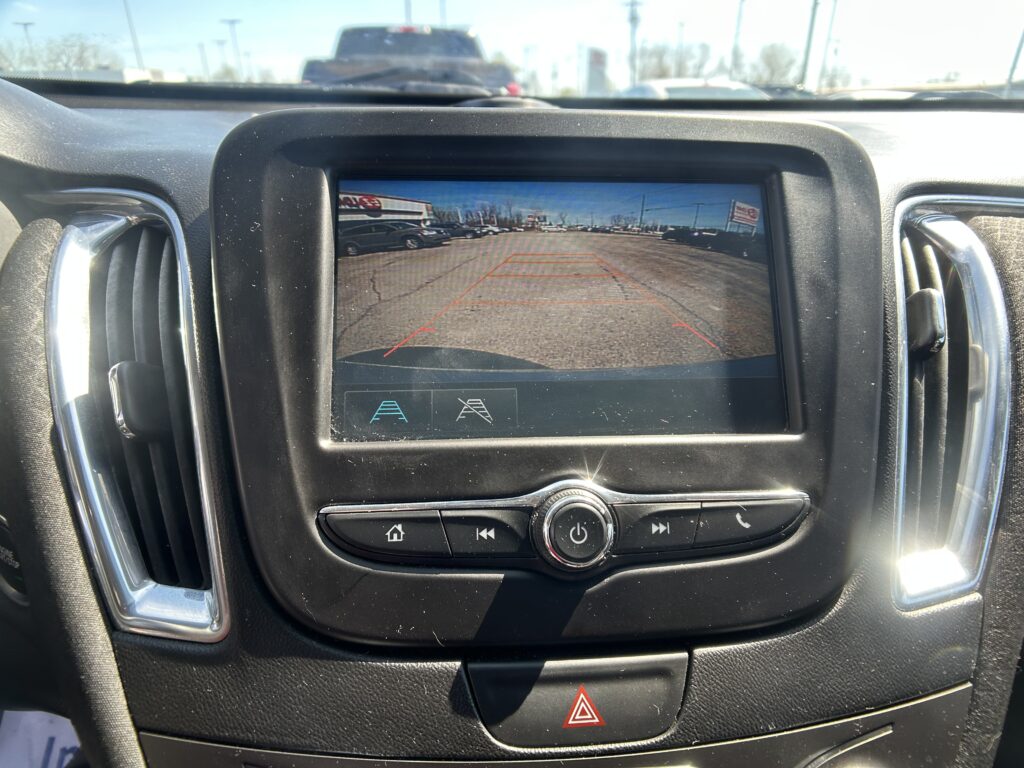 Rearview camera display on the car screen showing orange parking guide lines over a parking lot scene.