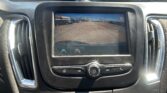 Rearview camera display on the car screen showing orange parking guide lines over a parking lot scene.
