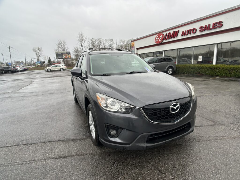 Grey Mercedes SUV in the foreground of a car lot, with EZ LOAN AUTO SALES storefront in the background on a cloudy, wet day.