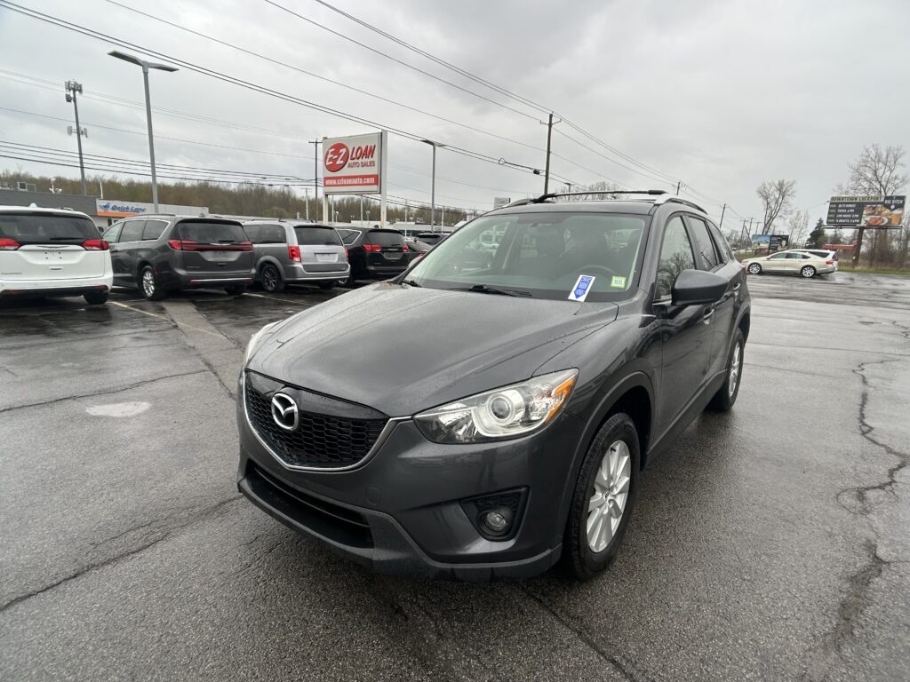 Gray SUV in the foreground at a crowded car dealership lot on an overcast day, with a large EZ Loan sign in the background.