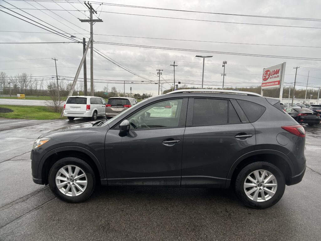 Gray SUV in the foreground of a wet parking lot with other cars and an EZ Loan Auto Sales sign in the distance under a cloudy sky.