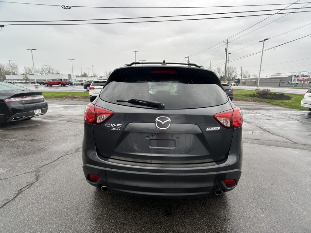 Rear view of a black Mazda CX-5 AWD in a wet parking lot with other cars and power lines in the background.