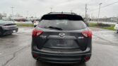 Rear view of a black Mazda CX-5 AWD in a wet parking lot with other cars and power lines in the background.