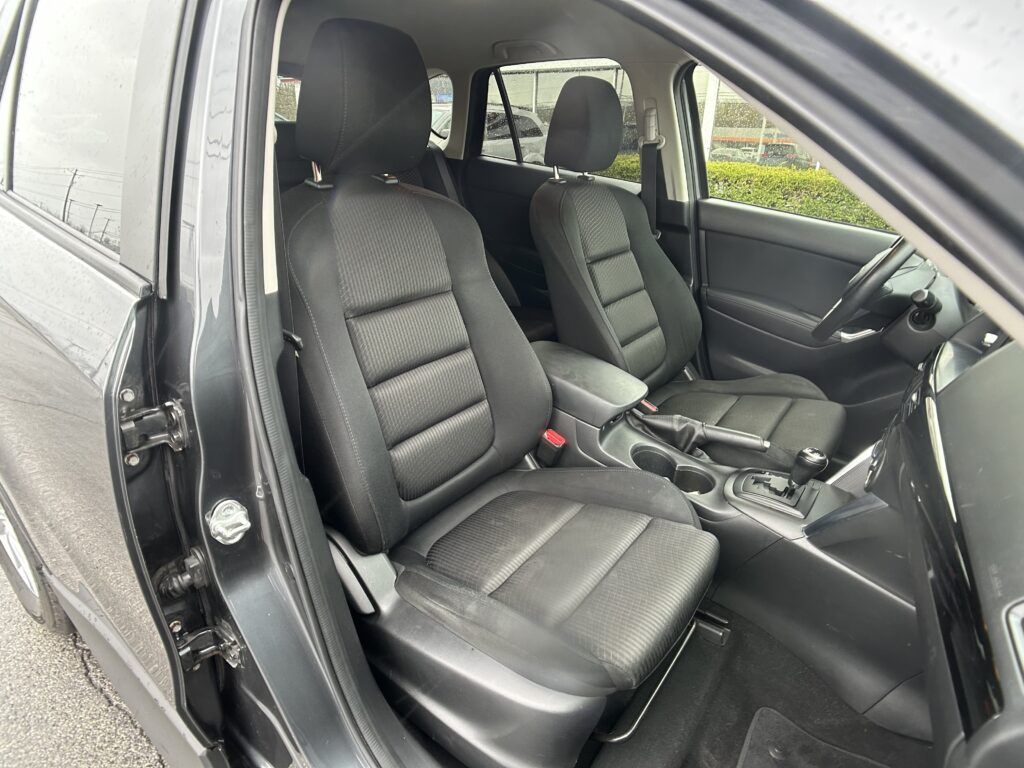 Front interior of a dark-cloth car seats area, passenger and driver seats visible, open driver's door showing seat belts and center console.