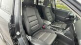 Front interior of a dark-cloth car seats area, passenger and driver seats visible, open driver's door showing seat belts and center console.