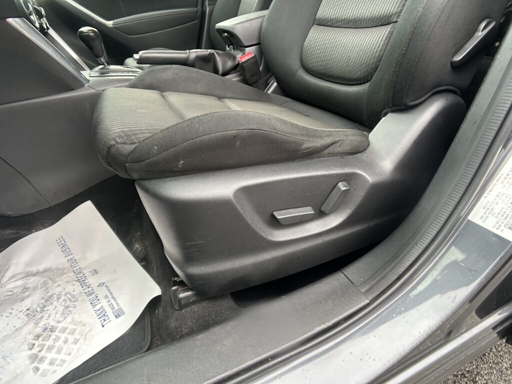 Front interior of a dark sedan with two black cloth seats, center console, and a floor protecting sheet partially visible near the door.