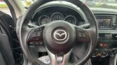 Inside view of a car cabin from the driver's seat, steering wheel centered, dashboard gauges visible, and a rain-speckled windshield in the background.