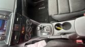 Interior of a dark SUV showing the center console with gear shifter, climate controls, cup holders, and a CX-5 branded floor mat near the driver seat with black fabric seats and side dash visible.