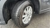 Close-up of a car wheel and tire, showing tread and alloy rim with dirt on the wheel well and fender nearby.