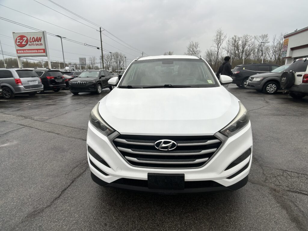 Front view of a white Hyundai SUV in a busy car dealership lot, with other vehicles and an E-Z Loan Auto Sales sign in the background.