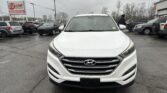 Front view of a white Hyundai SUV in a busy car dealership lot, with other vehicles and an E-Z Loan Auto Sales sign in the background.
