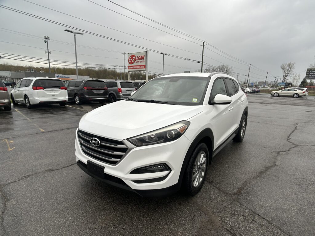 White Hyundai SUV in a dealership lot with other cars, a red E-Z LOAN Auto Sales sign in the background, and overcast skies.