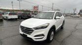 White Hyundai SUV in a dealership lot with other cars, a red E-Z LOAN Auto Sales sign in the background, and overcast skies.