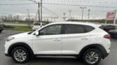 White SUV parked in a dealership lot with power lines overhead and an EZ LOAN Auto Sales sign in the background