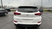 Rear view of a white Hyundai Tucson in a parking lot on a rainy, overcast day with other vehicles nearby.