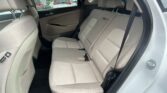 Back seat of a light-colored car with beige upholstery and headrests, viewed from the open rear door.