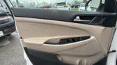 Interior of a car door with beige and black panels, power window controls and door handle; rainy parking lot visible through the open window.