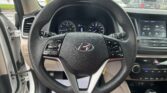 Steering wheel close-up in a Hyundai SUV with instrument cluster and touchscreen display visible on the right; raindrops on the windshield outside.