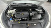 Open car hood showing engine bay with visible coolant reservoir and battery components under rainy conditions on a parking lot.