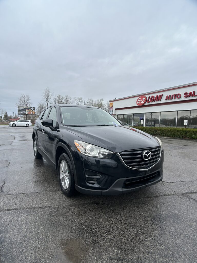 Black Mazda SUV in the dealership lot, with EZ Loan Auto Sales storefront and cloudy sky in the background, parked at an angle in the foreground.