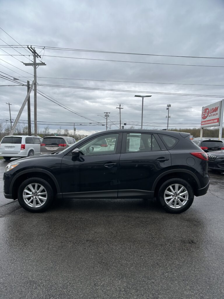 Dark gray SUV in foreground at a car dealership lot, with other cars, overhead power lines, and a red EZ Loan Auto Sales sign in the background under a cloudy sky