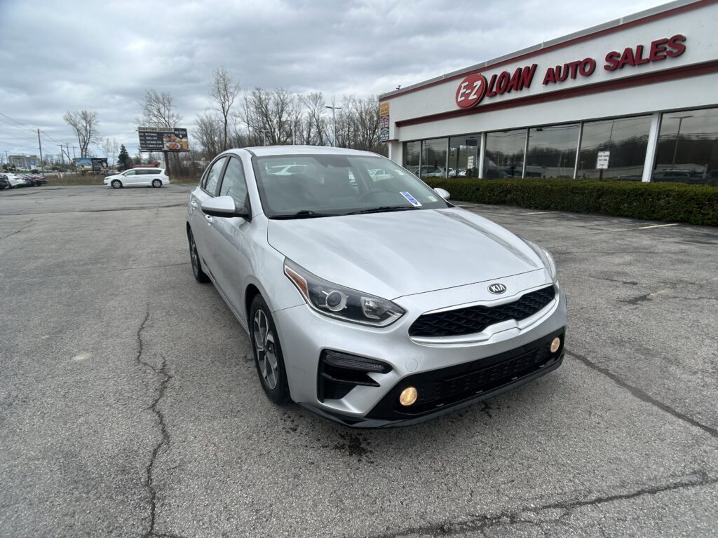 Silver Kia SUV in the foreground of a car lot, EZ Loan Auto Sales building in the background under a cloudy sky.