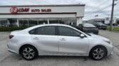 Side view of a silver sedan parked in front of EZ LOAN AUTO SALES with a white building and red trim, cloudy sky above.