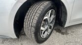 Close-up of a car wheel and tire mounted in the wheel well, showing a silver alloy rim and treaded tire on a light-gray vehicle.