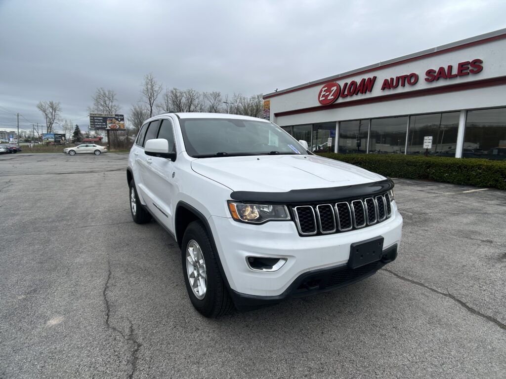 White Jeep Grand Cherokee SUV parked in a dealership lot in front of an EZ Loan Auto Sales building.