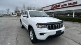 White Jeep Grand Cherokee SUV parked in a dealership lot in front of an EZ Loan Auto Sales building.
