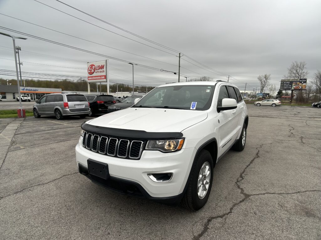 White SUV in a dealership lot on a cloudy day, with other cars and dealership signs in the background (E-Z Loan Auto Sales).