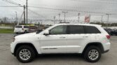 White Jeep Grand Cherokee in a parking lot with overhead power lines and a red EZ LOAN Auto Sales sign in the background, daytime.