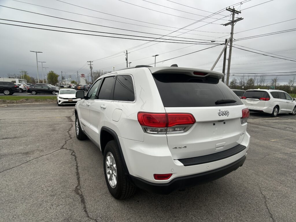 White Jeep SUV parked in a dealership lot with overhead power lines in the background.