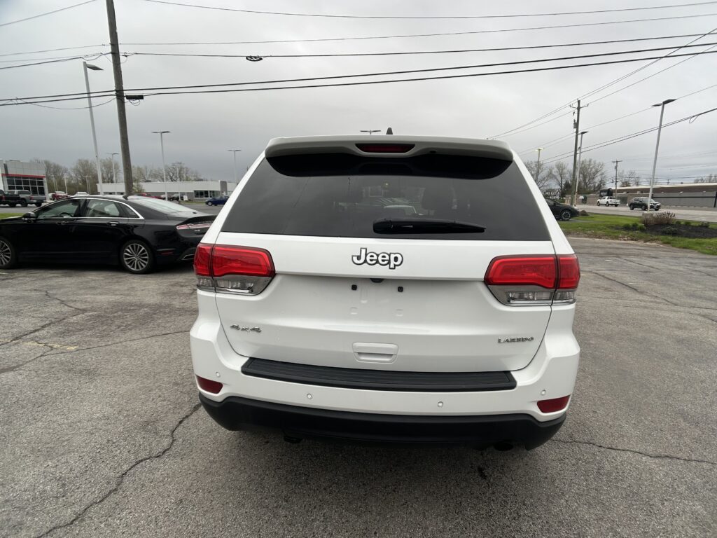 White Jeep SUV seen from the rear in a parking lot, with other cars and power lines in the background.