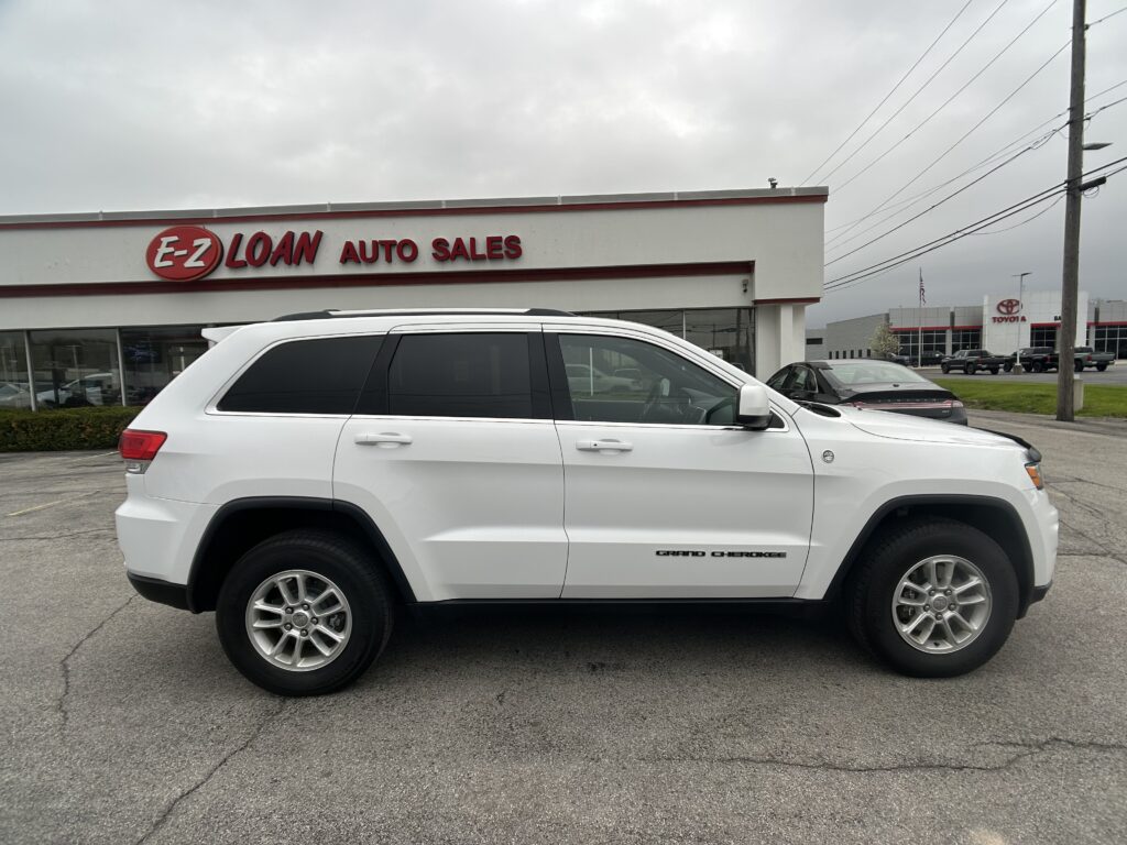 White SUV (Grand Cherokee) in front of E-Z LOAN AUTO SALES storefront; cloudy sky above, dealership sign visible.