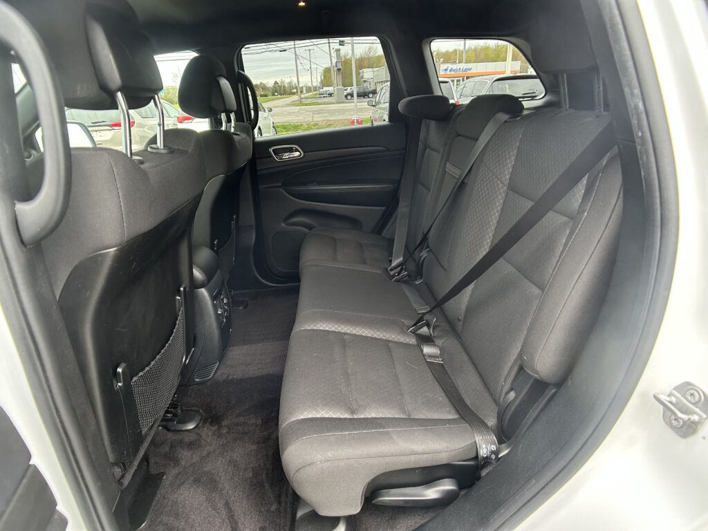Rear passenger area of a car with black fabric seats, three headrests, and visible seat belts; door panel and window view of a parking lot outside.
