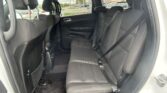 Rear passenger area of a car with black fabric seats, three headrests, and visible seat belts; door panel and window view of a parking lot outside.