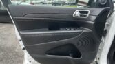 Interior of a car door panel with black texture, chrome handle, window controls, and a speaker; parking lot visible through the window.