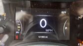 Car dashboard display showing 0 mph, outside temperature 52°F, odometer at 121,863 miles, with a red warning icon illuminated in the lower left corner and dust specks on the screen.