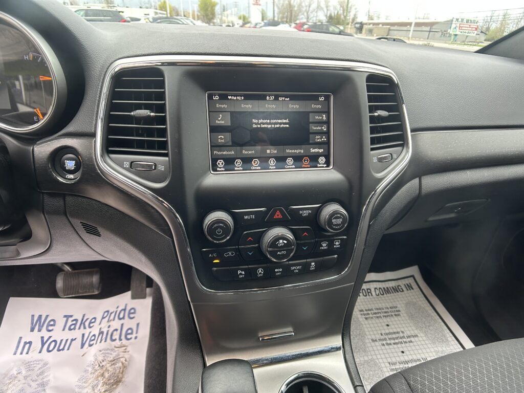 Interior of a car showing the center touchscreen and climate controls with a paper on the floor reading 'We Take Pride In Your Vehicle'.