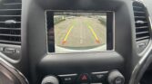 Car infotainment screen showing rearview camera view with parking lot, guiding lines, and the message 'Check entire surroundings'
