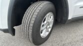 Front wheel of a light gray SUV, showing a treaded tire in the wheel well with a silver alloy rim
