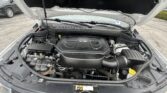 Car engine bay with hood open, showing V6 engine cover and surrounding components in a parking lot area