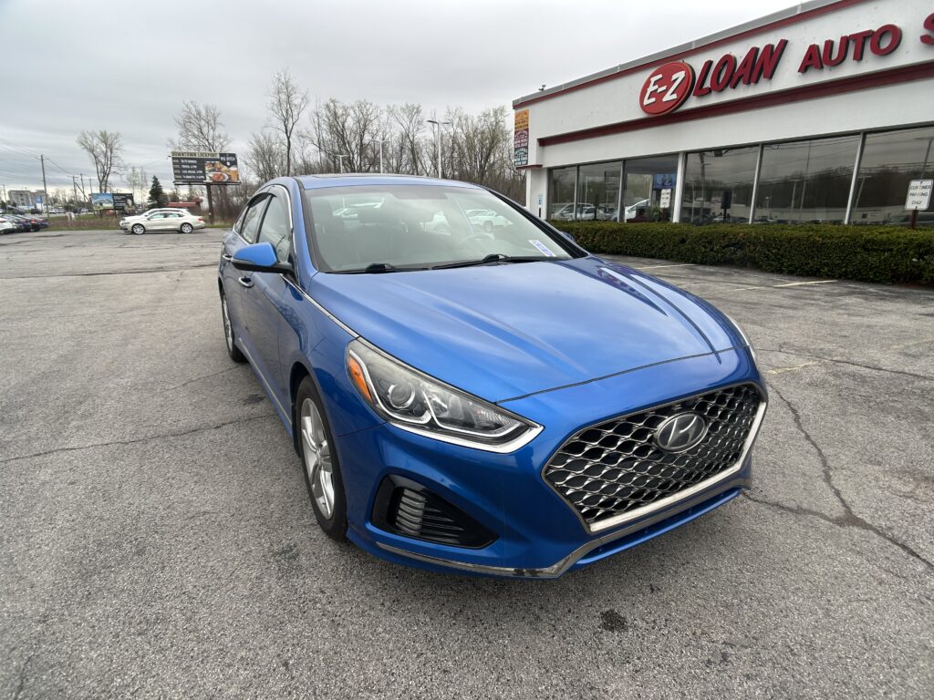 Blue Hyundai SUV parked diagonally in a dealership lot with EZ Loan Auto storefront in the background, glass showroom windows visible.