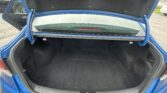 Open trunk of a blue sedan, showing a clean black cargo area with the rear windshield in view in a parking lot