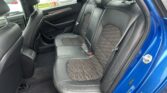 Rear interior of a blue car with black leather seats, headrests, and door panel visible on the left side.