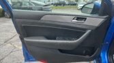 Open car door on the driver's side, showing door panel with window controls, outside a busy car lot of parked vehicles.