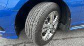 Close-up of a blue car's front wheel and fender, showing the tire tread and alloy rim on asphalt.