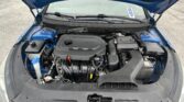 Under-hood view of a blue car, showing the engine bay with a plastic engine cover, battery on the right, and windshield with wipers in place.